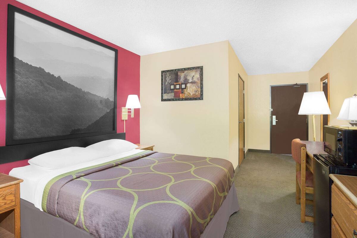 Ein Hotelzimmer mit einem großen Bett, einem Schreibtisch mit Computer, einem Sessel und einem Fernseher.