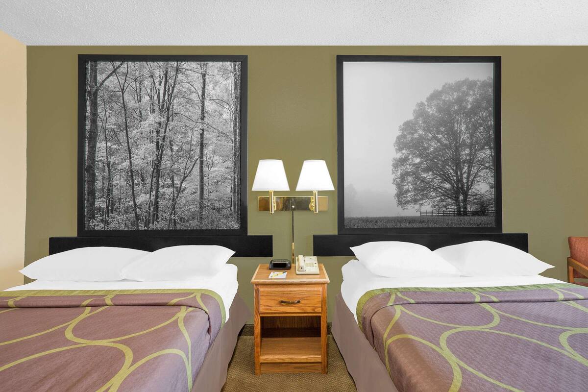 Ein Hotelzimmer mit zwei Betten, einem Nachttisch mit Lampen und zwei großen Bildern an der Wand.
