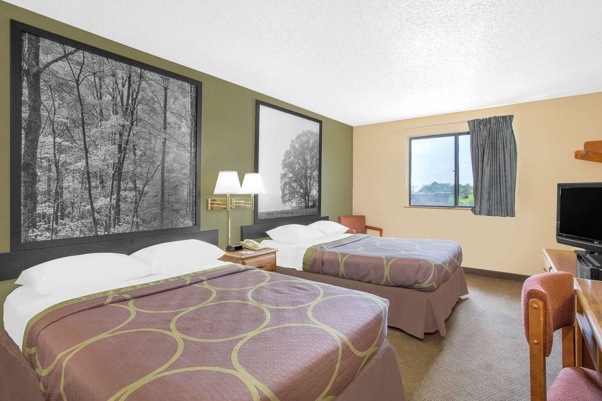 Ein Hotelzimmer mit zwei Betten, einem Fernseher, einem Schreibtisch und einem großen Fenster.