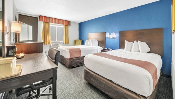 A hotel room with two beds, a desk, a chair, a lamp, and a window with curtains. - City Centre Inn at Newport News (Newport News)