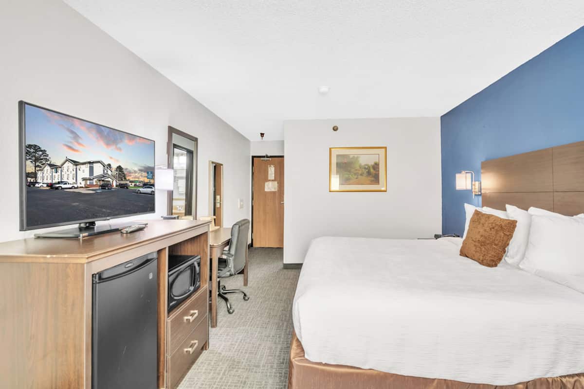 A hotel room with a large bed, a desk with a television, a refrigerator, and a chair.