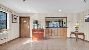 A hotel lobby with a reception desk, a coffee machine, a small table with a lamp, and a large window. - City Centre Inn at Newport News (Newport News)