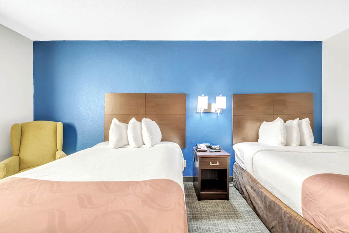 A hotel room with two beds, a small bedside table with a phone, and a chair.