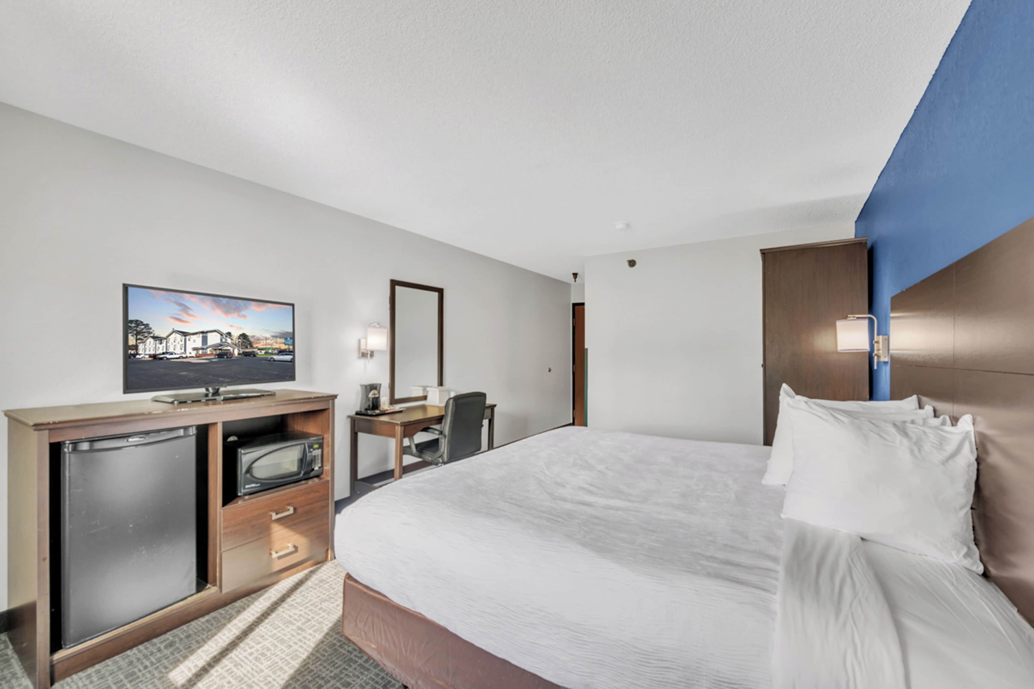 A hotel room with a bed, a desk, a television, and a minibar.