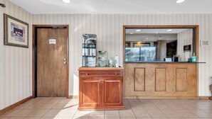 A hotel reception area with a wooden cabinet, a coffee machine, and a framed picture on the wall. - City Centre Inn at Newport News (Newport News)