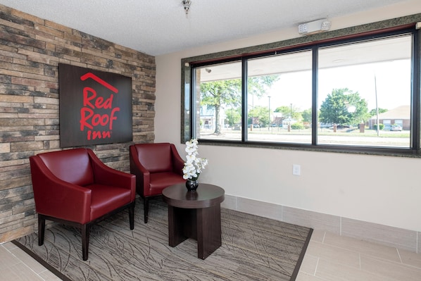 Vestíbulo de Red Roof Inn con una pared de piedra, dos sillones rojos, una mesita con un jarrón de flores y un ventanal con vista a la calle.