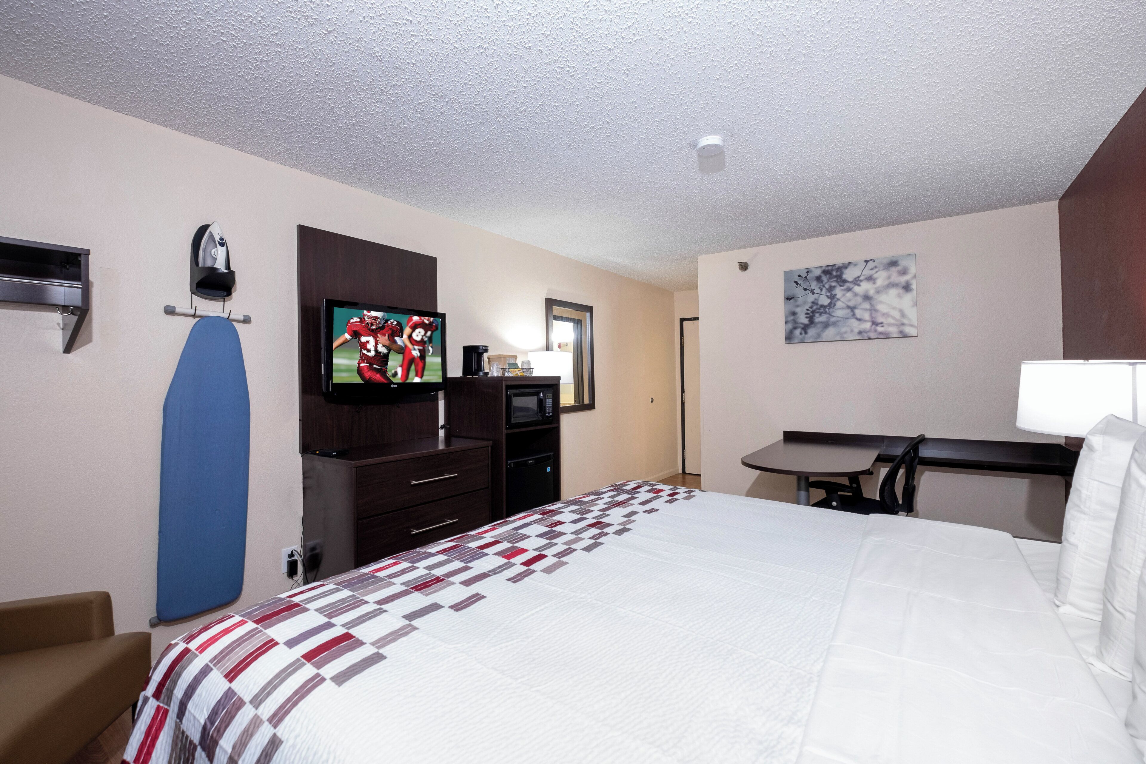 A hotel room with a bed, a desk, a television, a microwave, and a coffee maker.