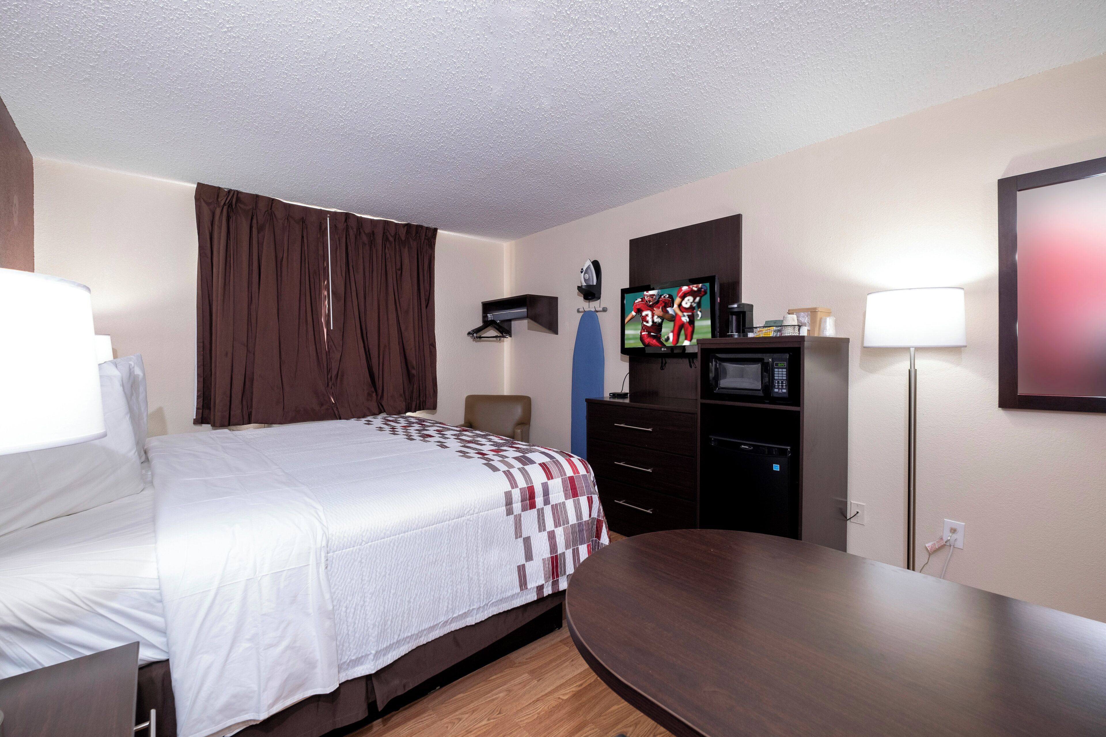 Una habitación de hotel con cama, escritorio, silla, televisión, microondas y lámpara.