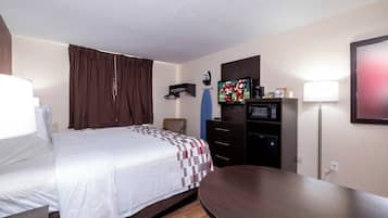 Una habitación de hotel con cama, escritorio, silla, televisión, microondas y lámpara.