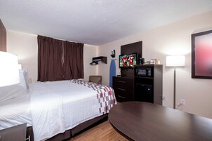 Una habitación de hotel con cama, escritorio, silla, televisión, microondas y lámpara.
