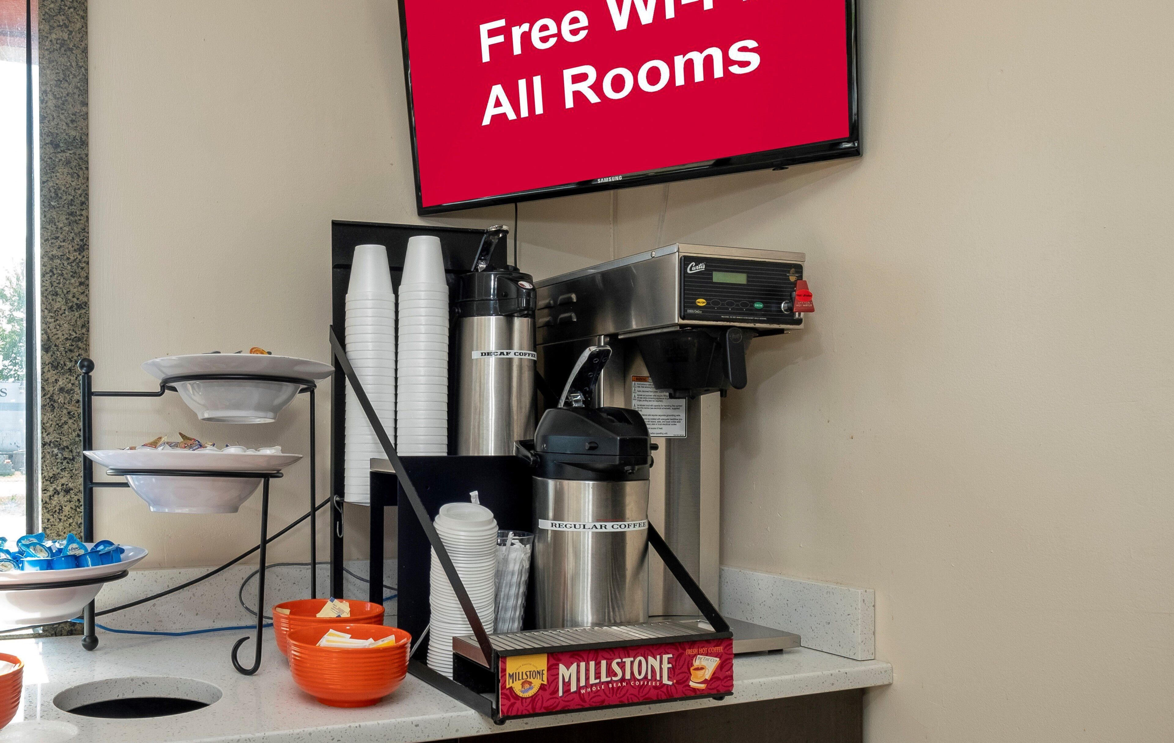 A coffee station with a coffee machine, disposable cups, and a sign indicating free Wi-Fi availability.