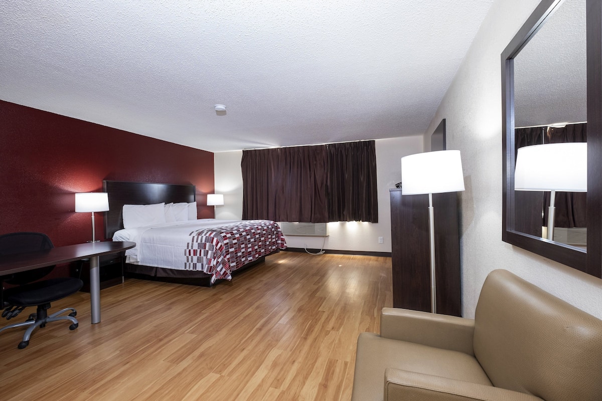 Habitación de hotel con cama, escritorio, silla y un espejo grande.