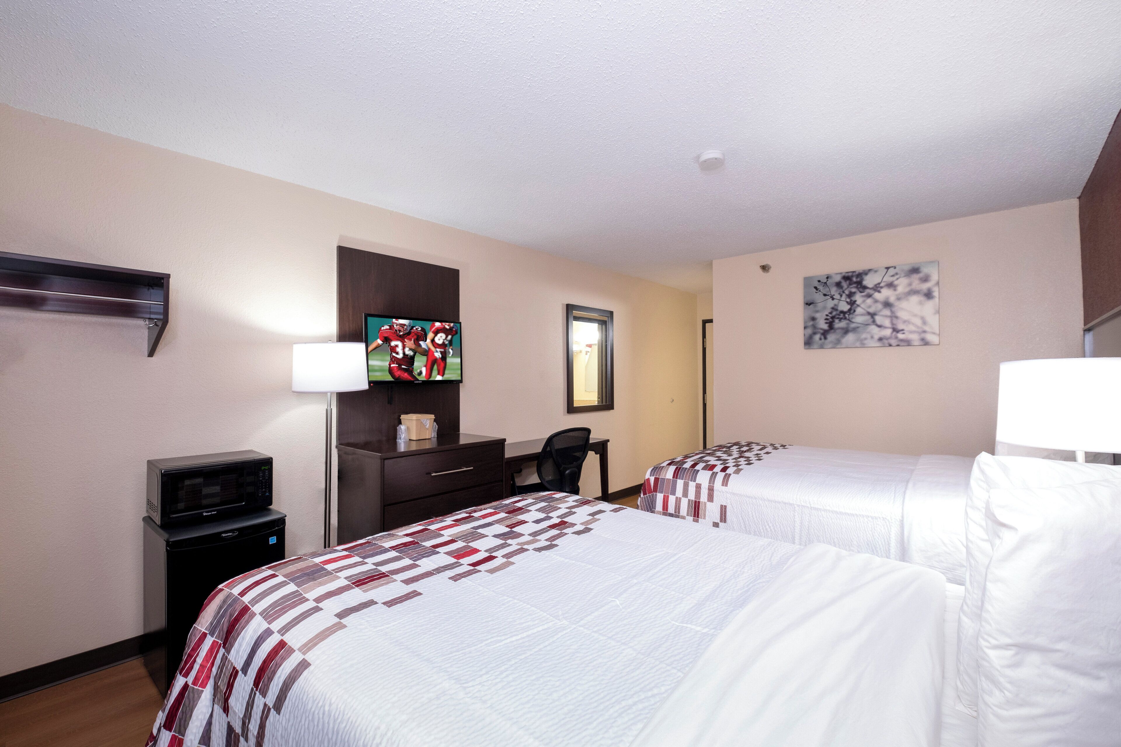 Habitación de hotel con dos camas, un escritorio, televisor, microondas y un mueble pequeño.