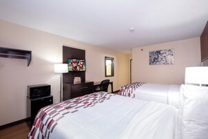 Habitación de hotel con dos camas, un escritorio, televisor, microondas y un mueble pequeño.