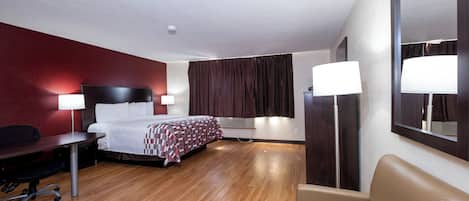 A hotel room with a bed, desk, chair, and a large mirror.