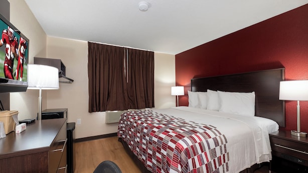 Une chambre d’hôtel comprenant un lit, des tables de chevet, un bureau, une chaise, une télévision et une fenêtre avec des rideaux.