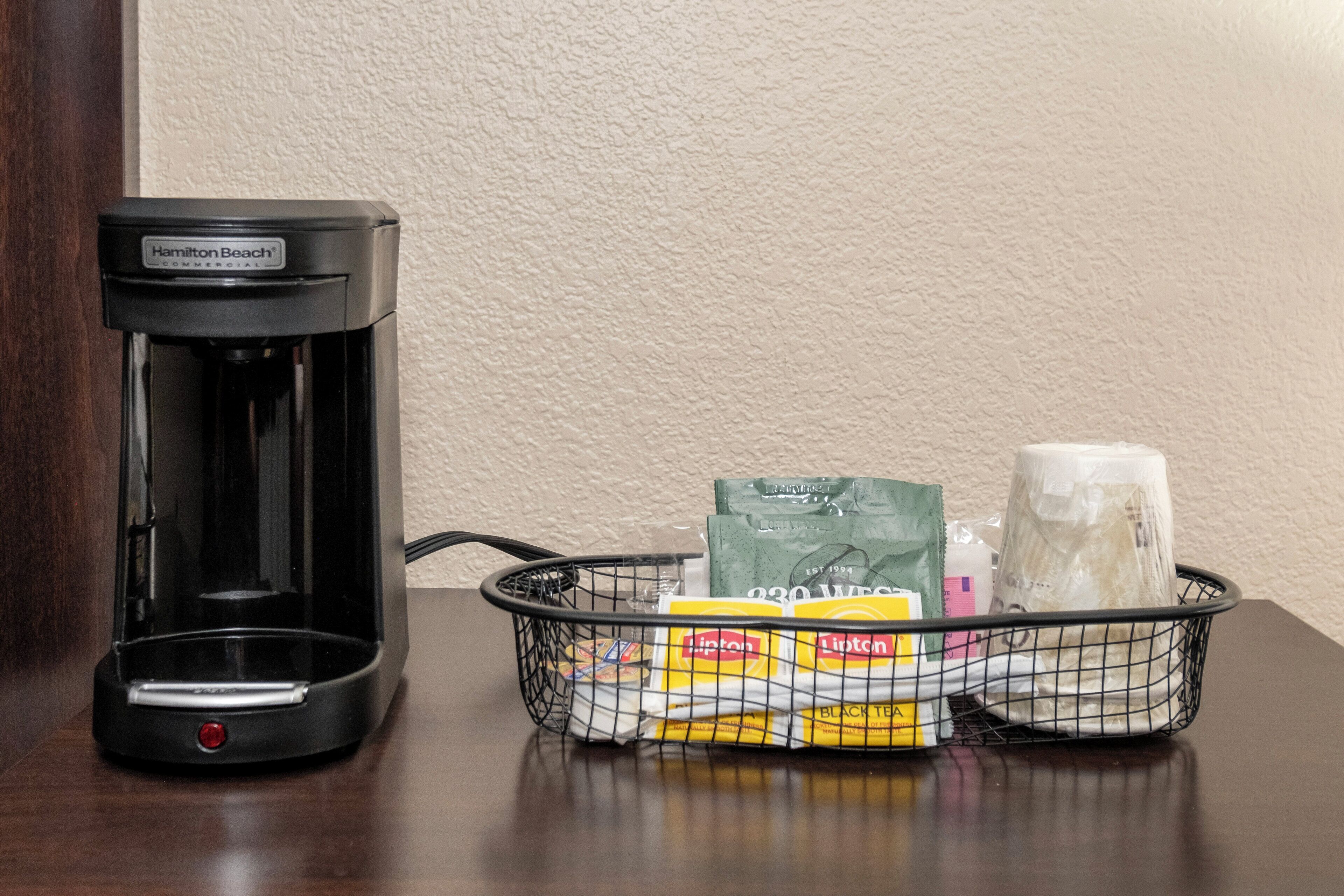 A Hamilton Beach commercial coffee maker and a basket containing Lipton tea bags and a glass.