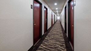 Un couloir d’hôtel avec des portes des deux côtés, une moquette à motifs et un plafond doté d’un éclairage encastré.