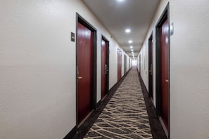 Ein Hotelgang mit Türen an beiden Seiten, einem gemusterten Teppich und einer Decke mit eingelassener Beleuchtung.