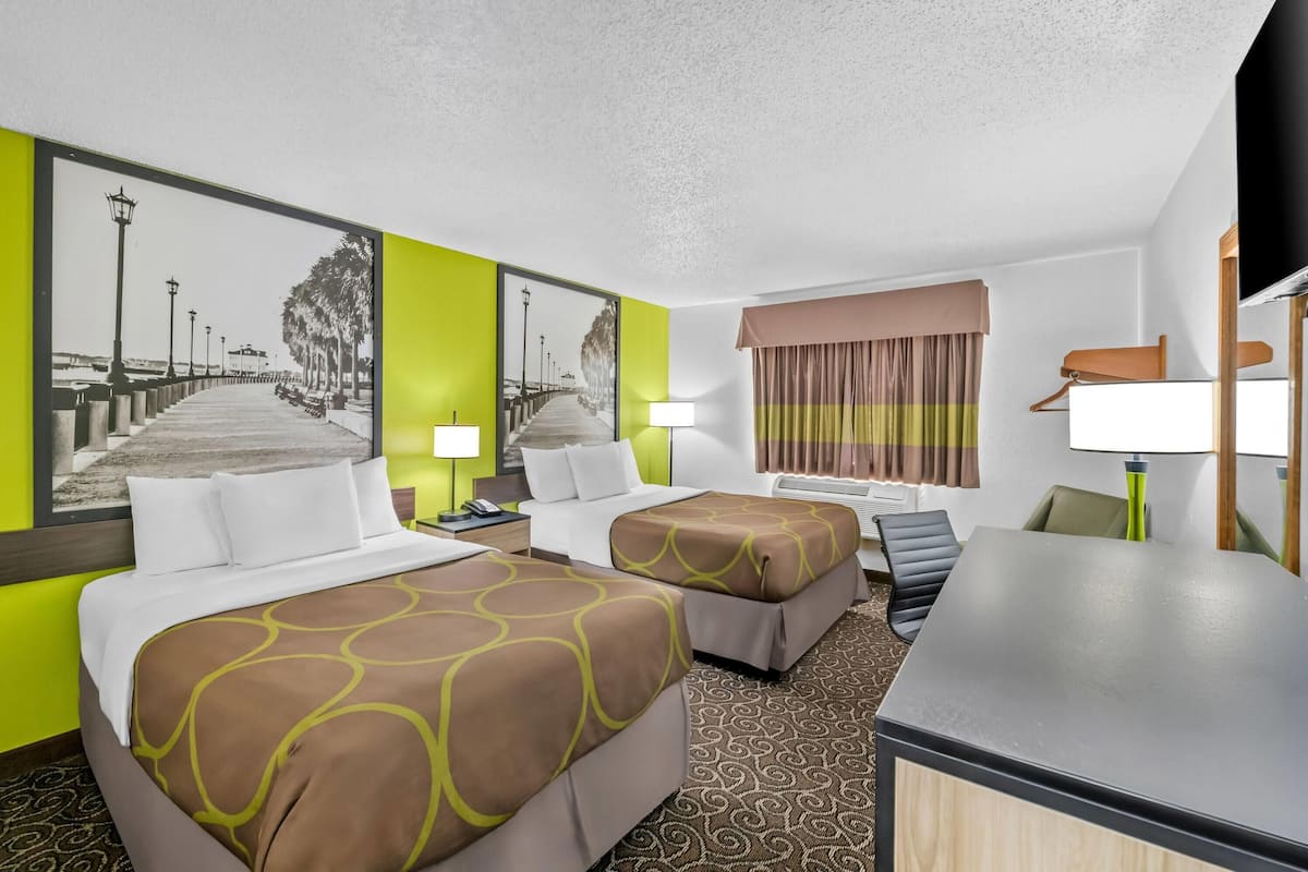 Quarto de hotel com duas camas, uma escrivaninha e uma janela grande com cortinas.