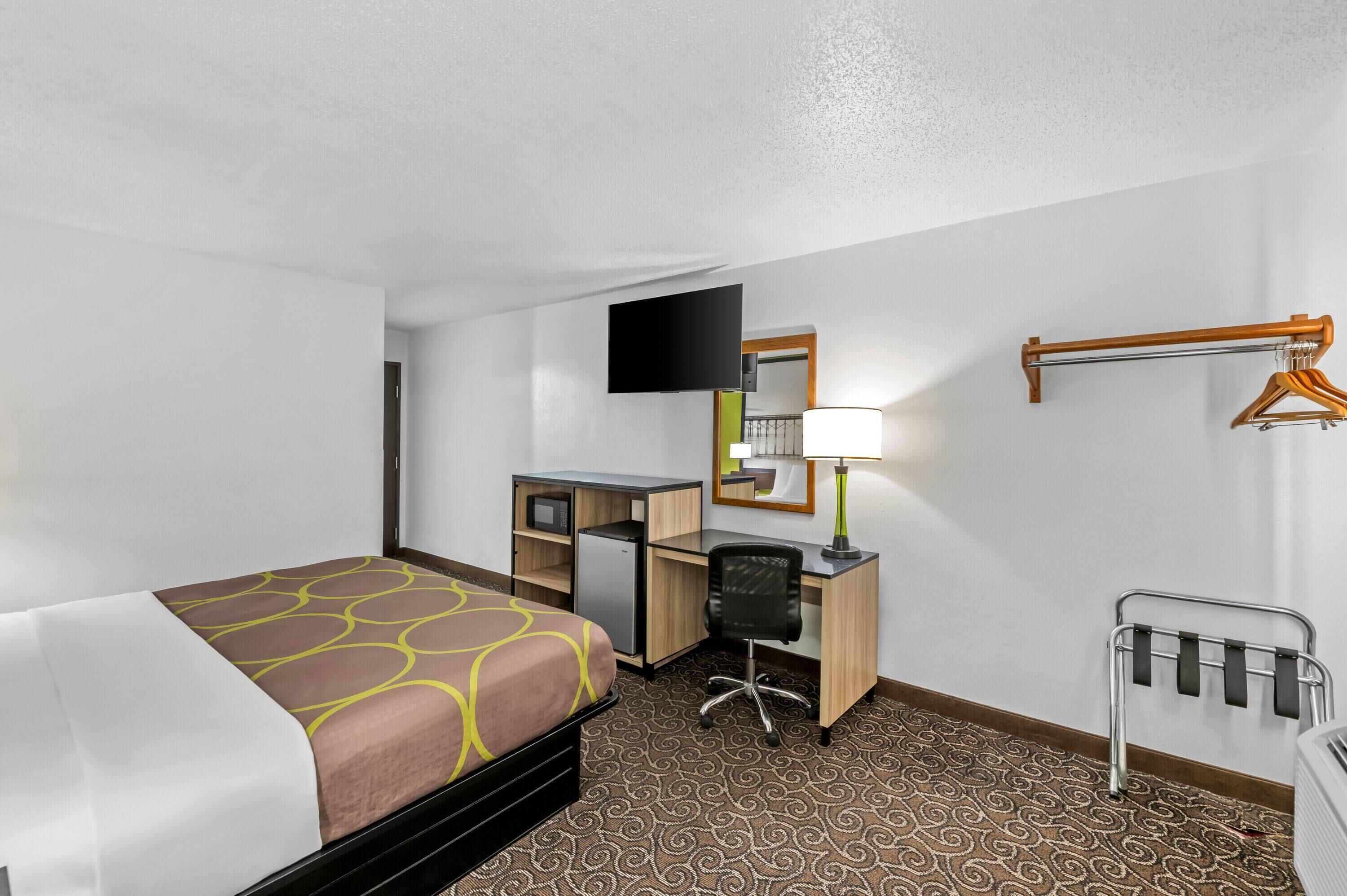 A hotel room with a bed, desk, chair, TV, lamp, and a coat rack.