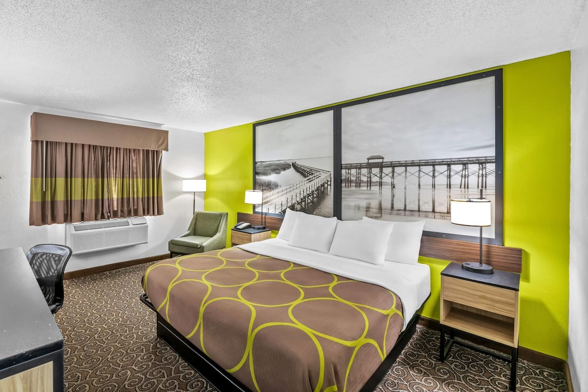 Quarto de hotel com cama, escrivaninha, cadeira, janela com vista para um cais e ar-condicionado fixado na parede.