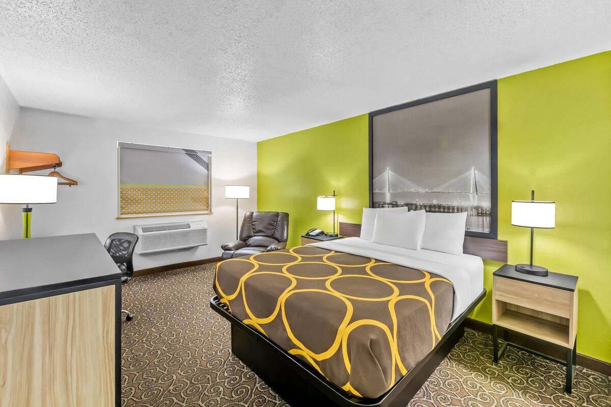 Quarto de hotel com cama, escrivaninha, cadeira e duas mesas de cabeceira com luminárias.