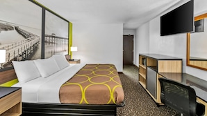 Una habitación de hotel con una cama, un escritorio, un televisor y un cuadro de un muelle.
