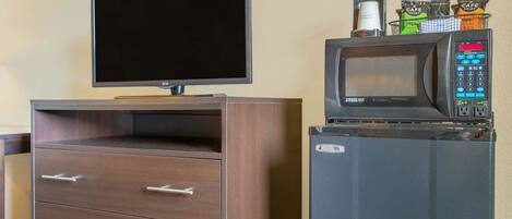 A flat-screen TV mounted on a wooden cabinet with drawers, and a microwave on top of a refrigerator.