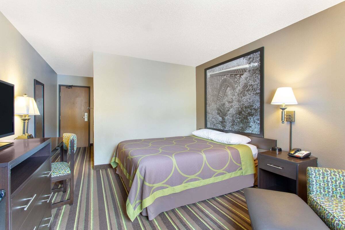 Une chambre d’hôtel comprenant un lit, un bureau avec une lampe, une chaise, une table de chevet avec une lampe et un grand tableau encadré au mur.