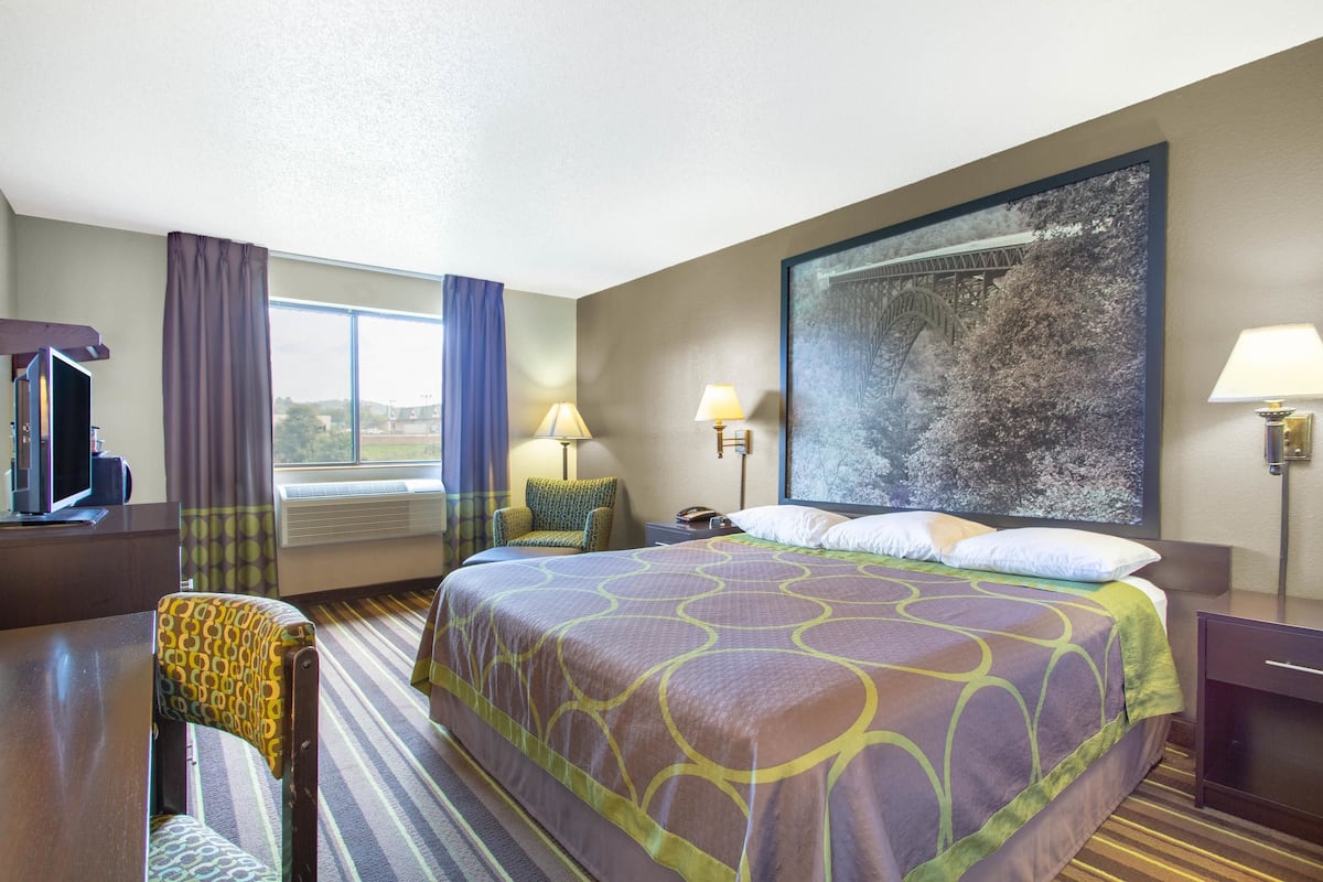 Une chambre d’hôtel avec un grand lit, un bureau, une chaise, une télévision et une fenêtre avec des rideaux.