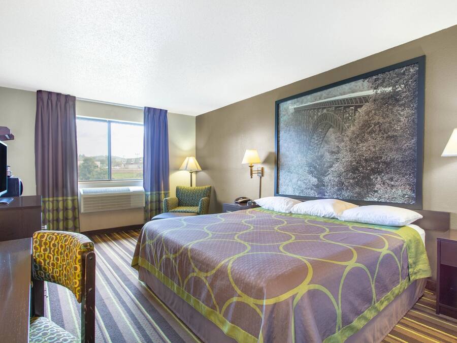 Une chambre d’hôtel avec un grand lit, un bureau, une chaise, une télévision et une fenêtre avec des rideaux.