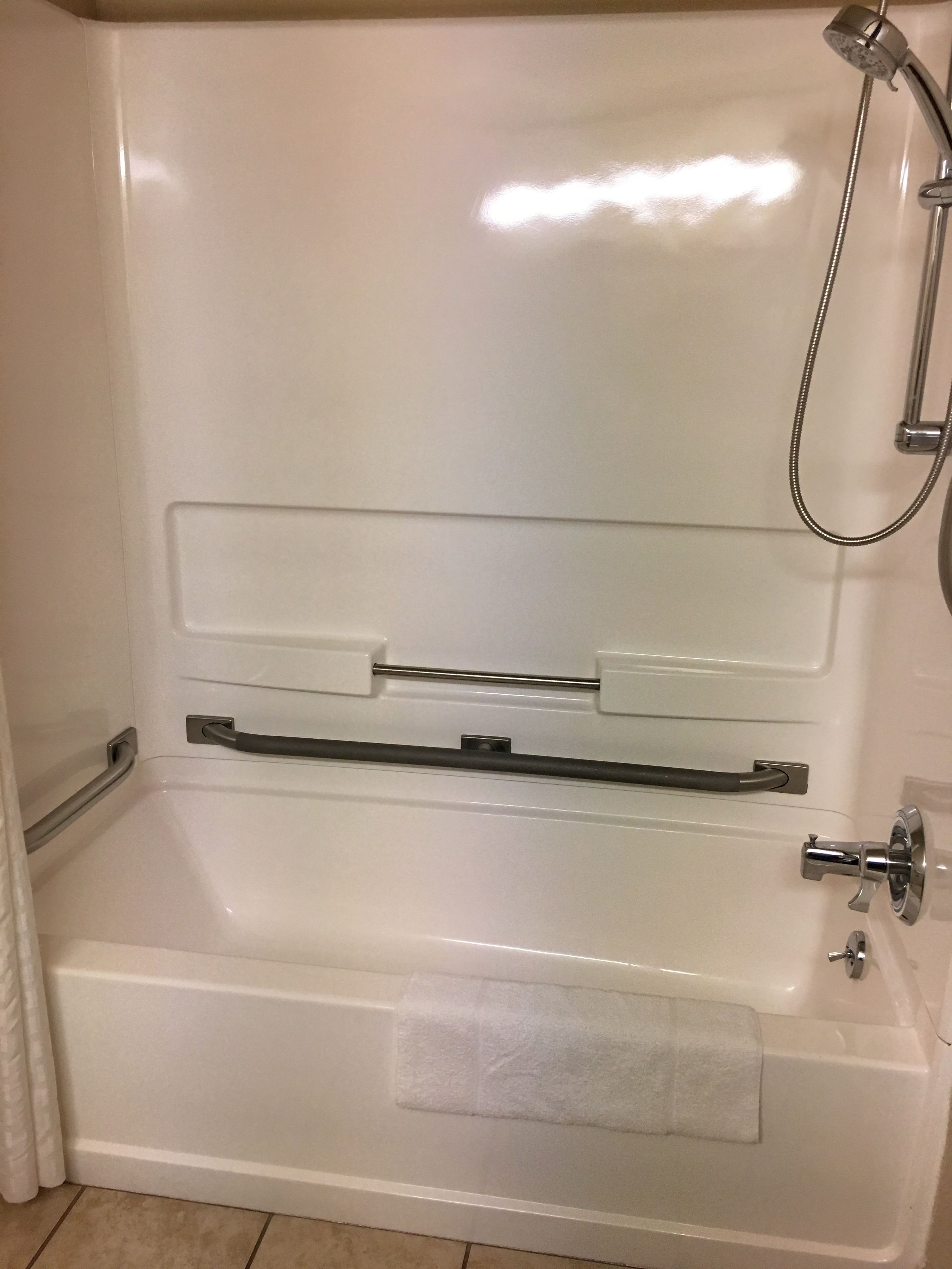 A white bathtub with a shower head, a towel rack, and a towel on the floor.