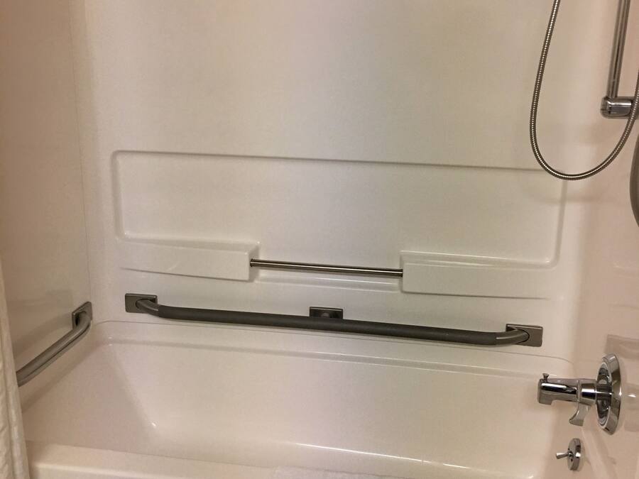 A white bathtub with a shower head, a towel rack, and a towel on the floor.