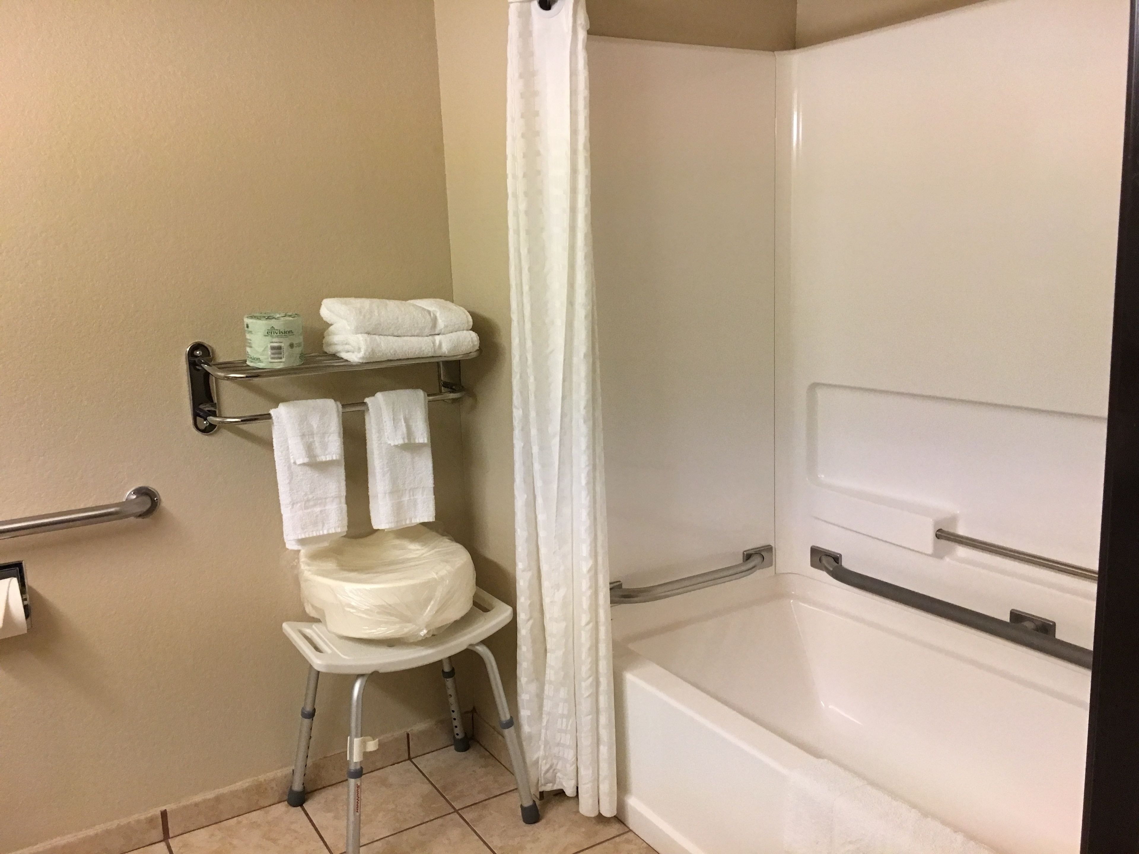 A bathroom with a white toilet, a shower with a white curtain, a grab bar, and a towel rack with folded towels.