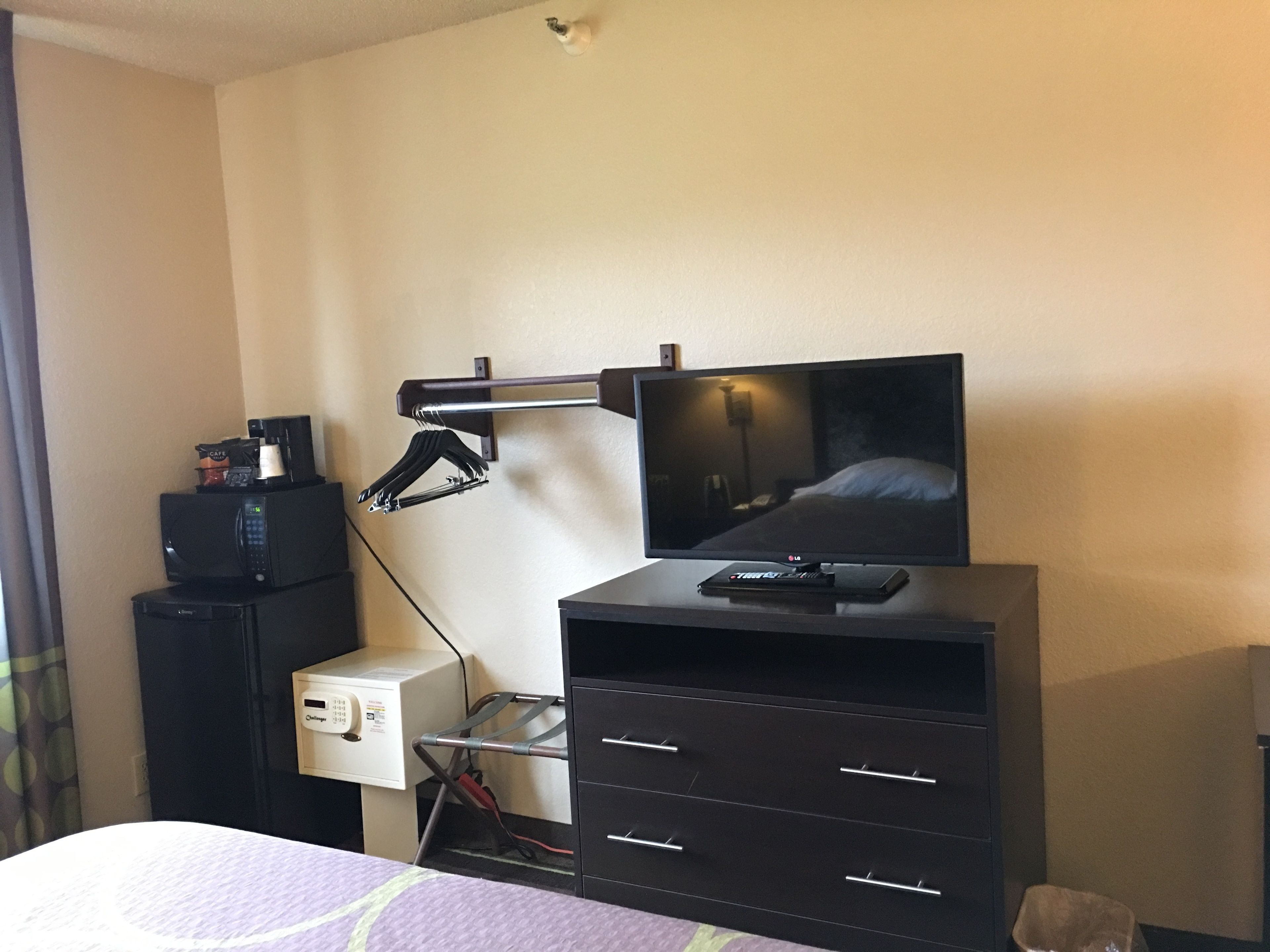 Una habitación de hotel con una cama, un televisor sobre un soporte, una cafetera y un mueble pequeño.