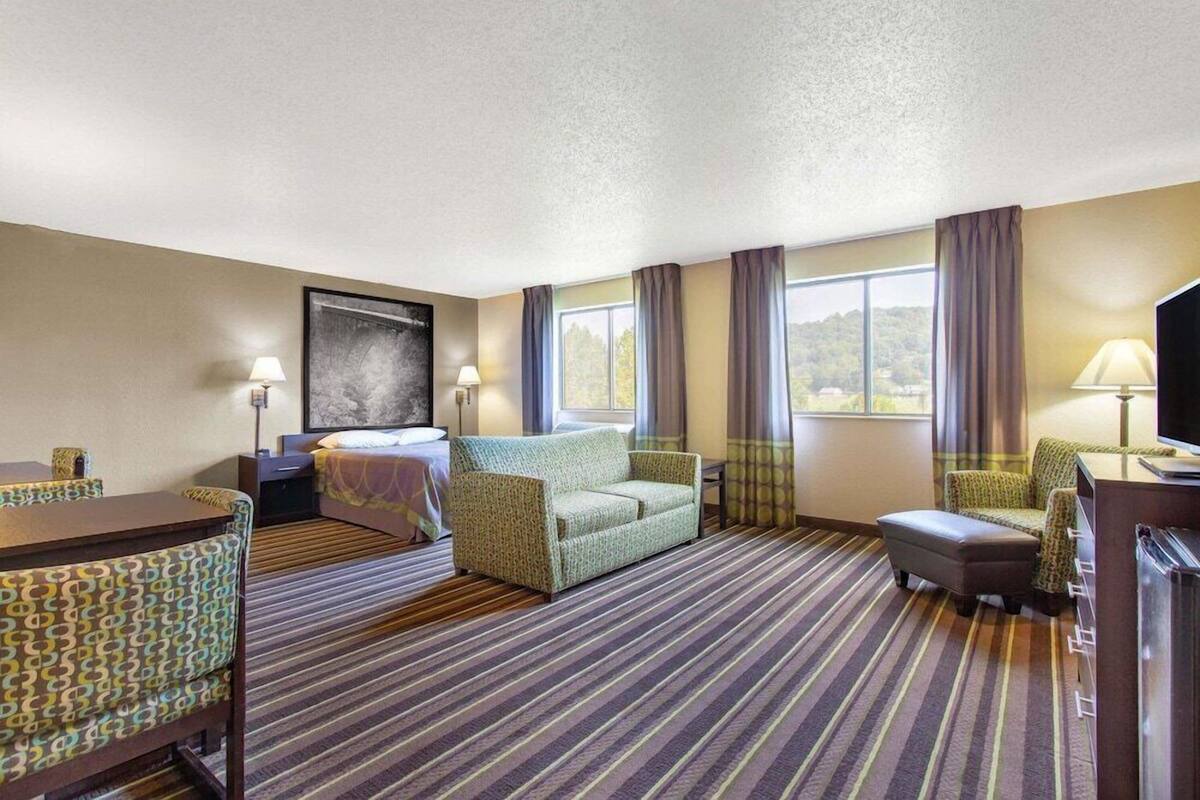 Une chambre d’hôtel avec un lit, un canapé, un bureau, une télévision et une fenêtre avec des rideaux.