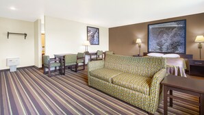 Een hotelkamer met een gestreept tapijt, een bank, een eettafel met stoelen, een bed met hoofdeinde en twee wandlampen.