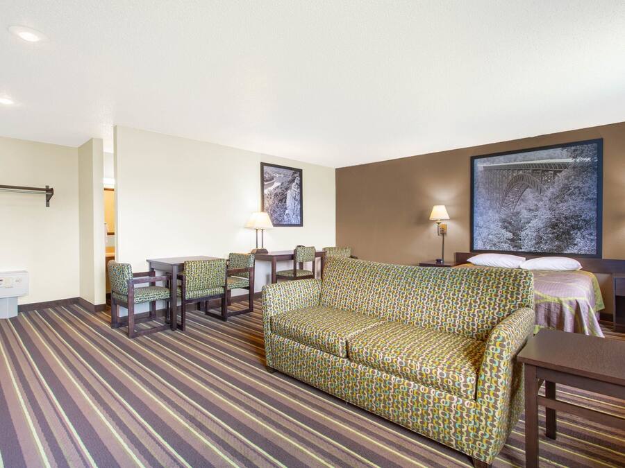 A hotel room with a striped carpet, a sofa, a dining table with chairs, a bed with a headboard, and two wall-mounted lamps.