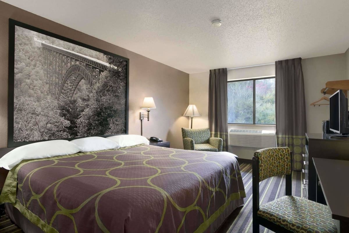 Une chambre d’hôtel avec un grand lit, un bureau avec une chaise, une télévision, une fenêtre avec des rideaux et une lampe fixée au mur.