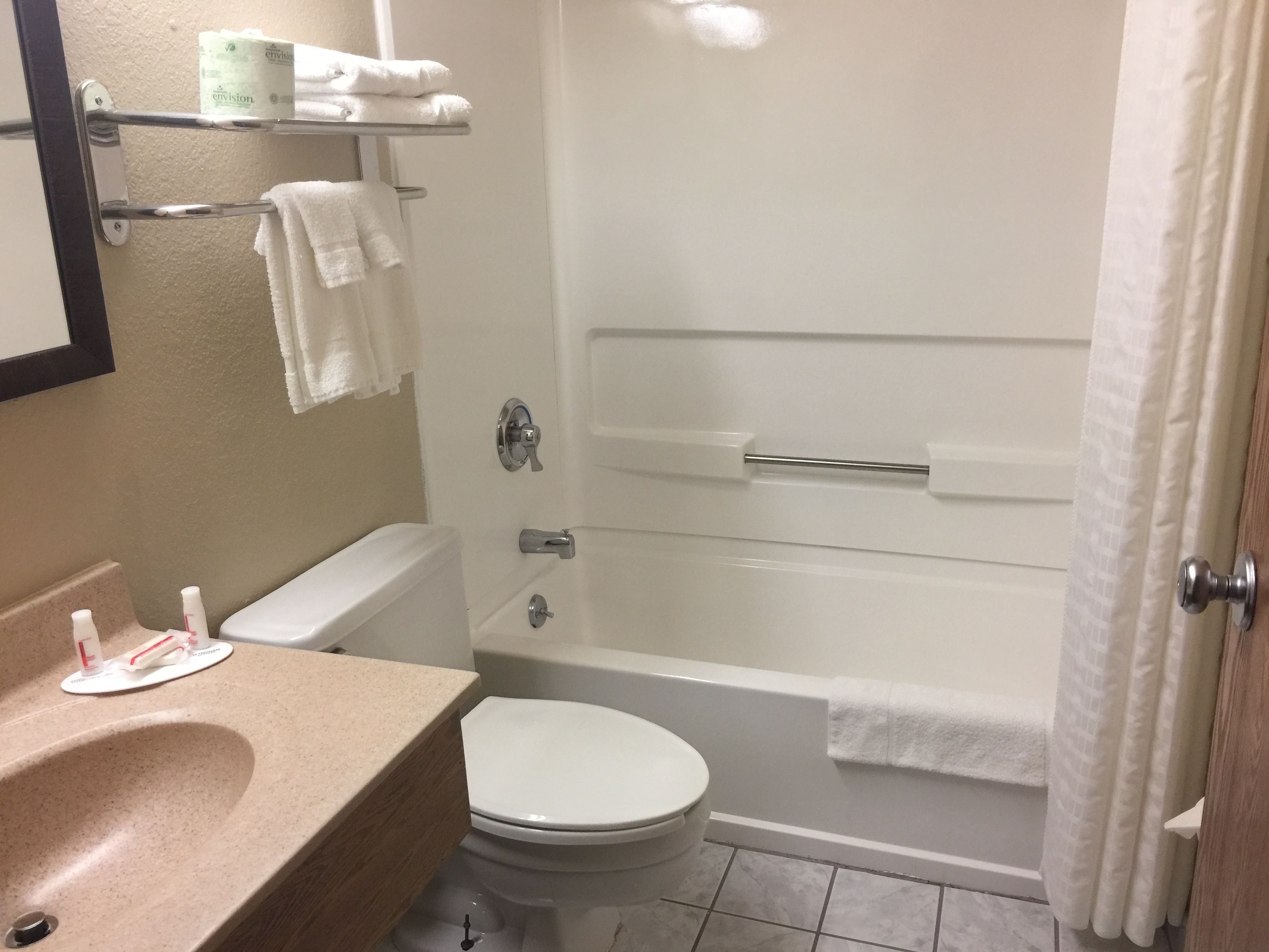 A bathroom with a toilet, sink, and bathtub. There are towels and toilet paper on the wall.
