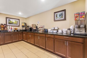 Una cocina de hotel con armarios de madera, una zona de café y una barra para el desayuno.