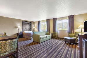 Een hotelkamer met een bed, twee sofa's, een bureau en een televisie.