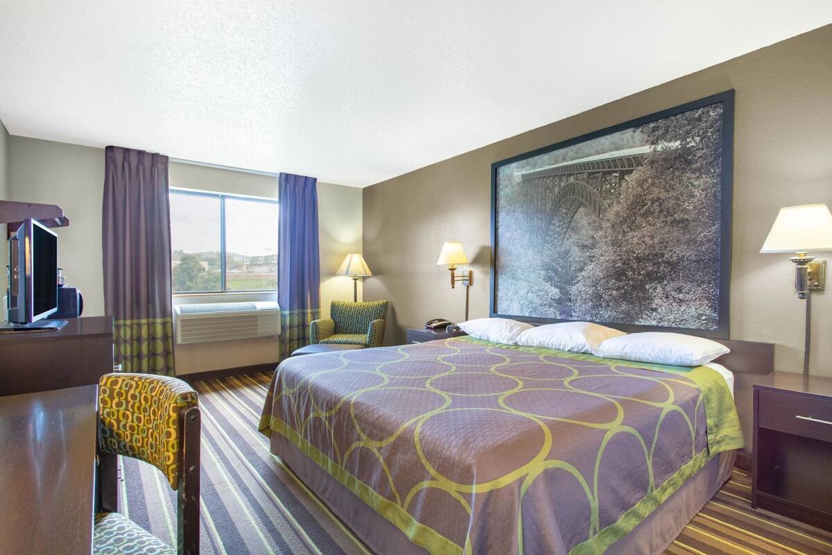 Une chambre d’hôtel avec un grand lit, un bureau avec un ordinateur, une chaise, deux lampes de chevet et une grande fenêtre avec des rideaux.