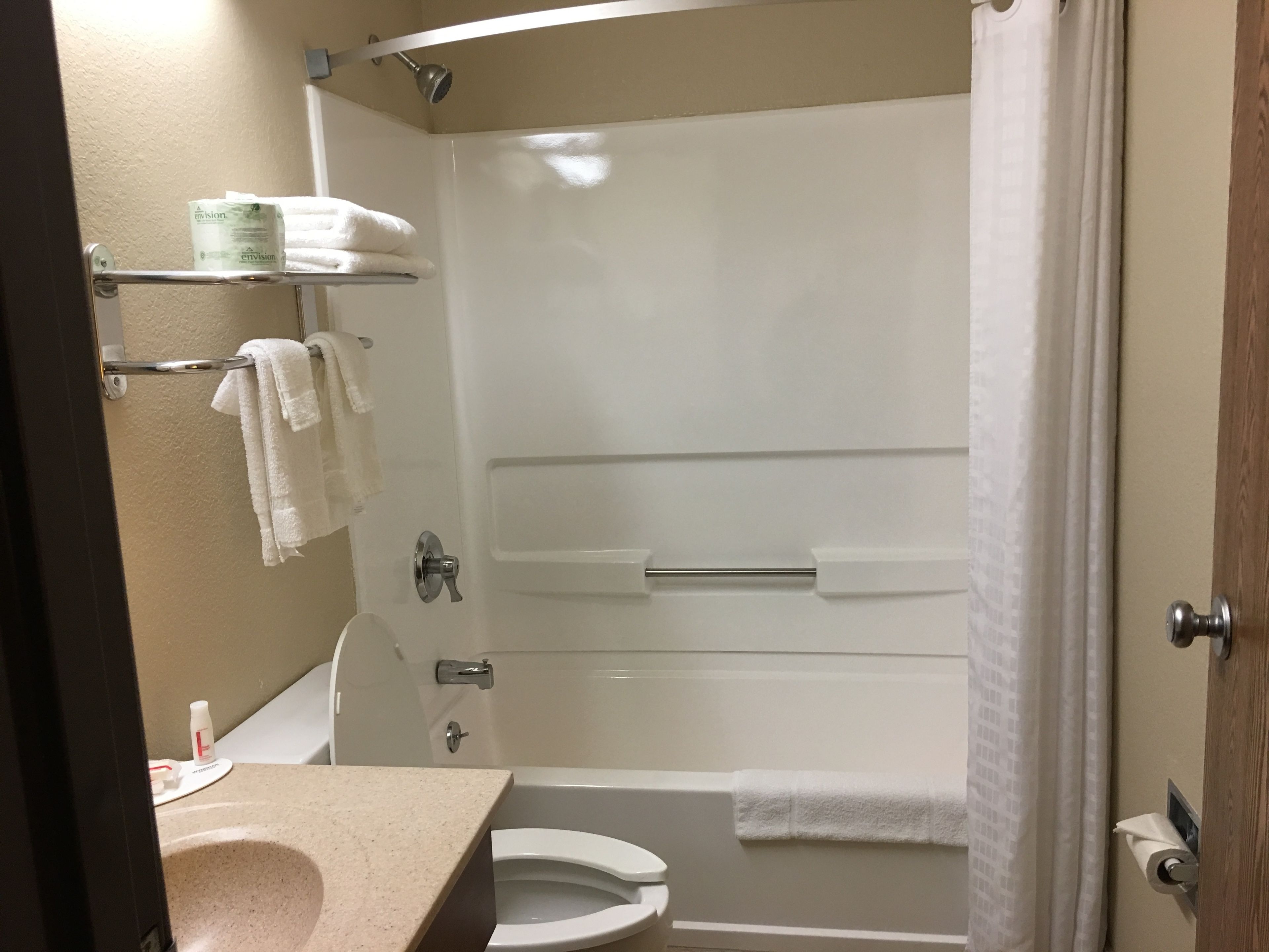 A bathroom with a toilet, sink, and shower area. There are towels and toiletries on shelves.