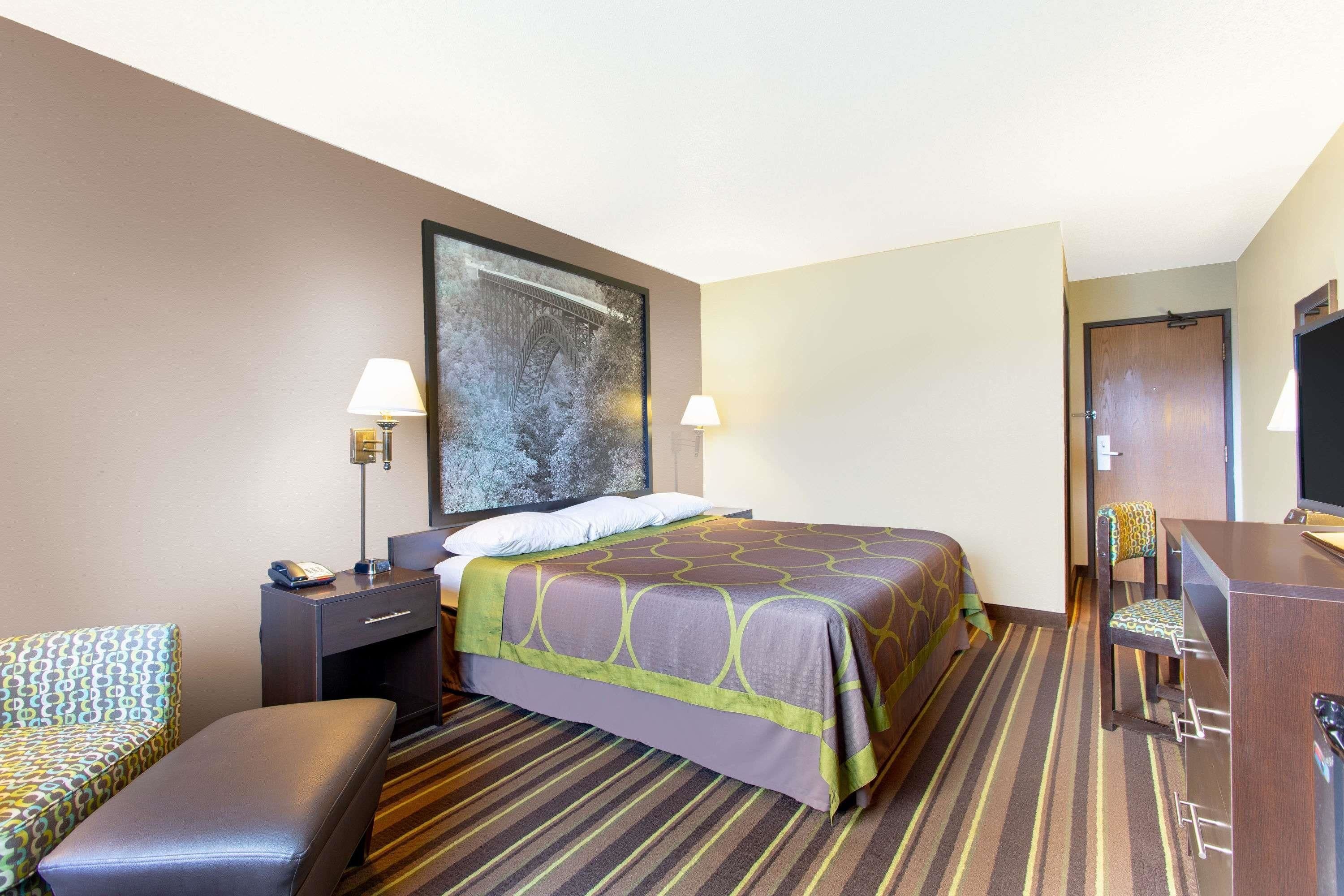 Habitación de hotel con cama, escritorio, silla, lámpara y un cuadro grande en la pared.