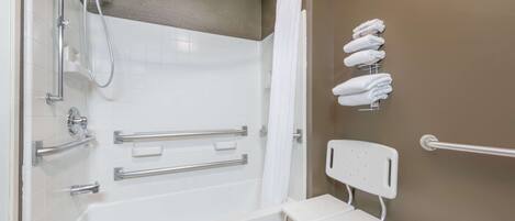 A bathroom with a walk-in shower, grab bars, a bench, and a towel rack.