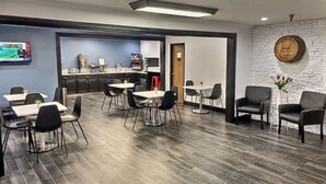 A modern dining area with tables and chairs, a kitchen in the background, and a brick wall with a clock. - Super 8 by Wyndham Georgetown (Georgetown)