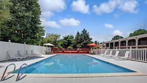 Una piscina rectangular con superficie de agua azul cristalina, rodeada de sillones blancos y una cerca blanca.