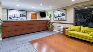 Zona de recepción con un mostrador de madera, una planta en maceta, un sofá amarillo y dos cuadros colgados en la pared.